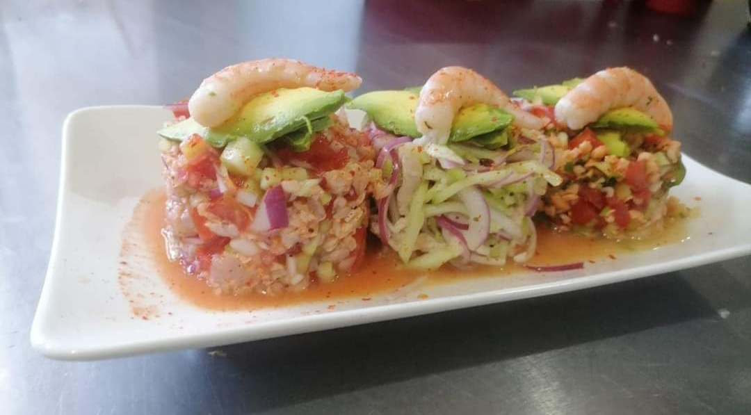 Restaurante Mariscos la Iguana sirviendo camarones al ajillo en plato de cerámica, fondo de cocina abierta