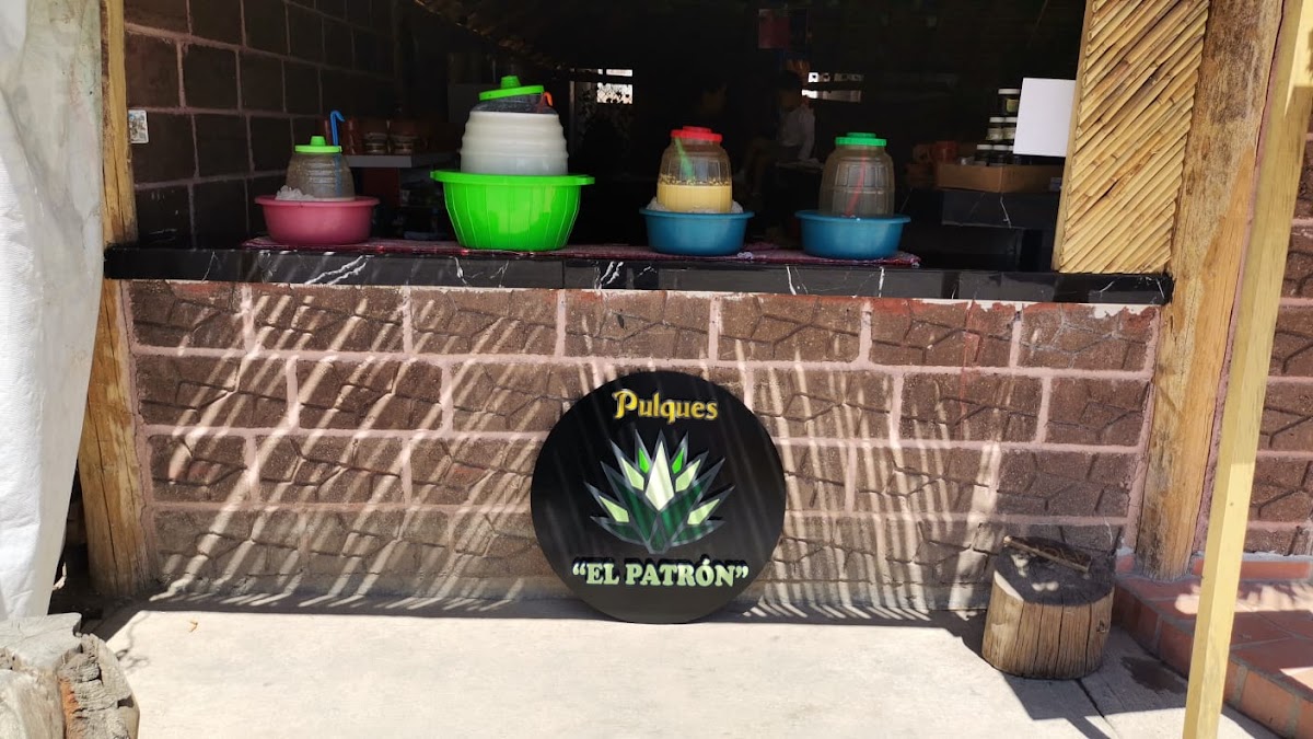Pulques el Patrón sirviendo un vaso de pulque tradicional, barra de madera y botellas alineadas