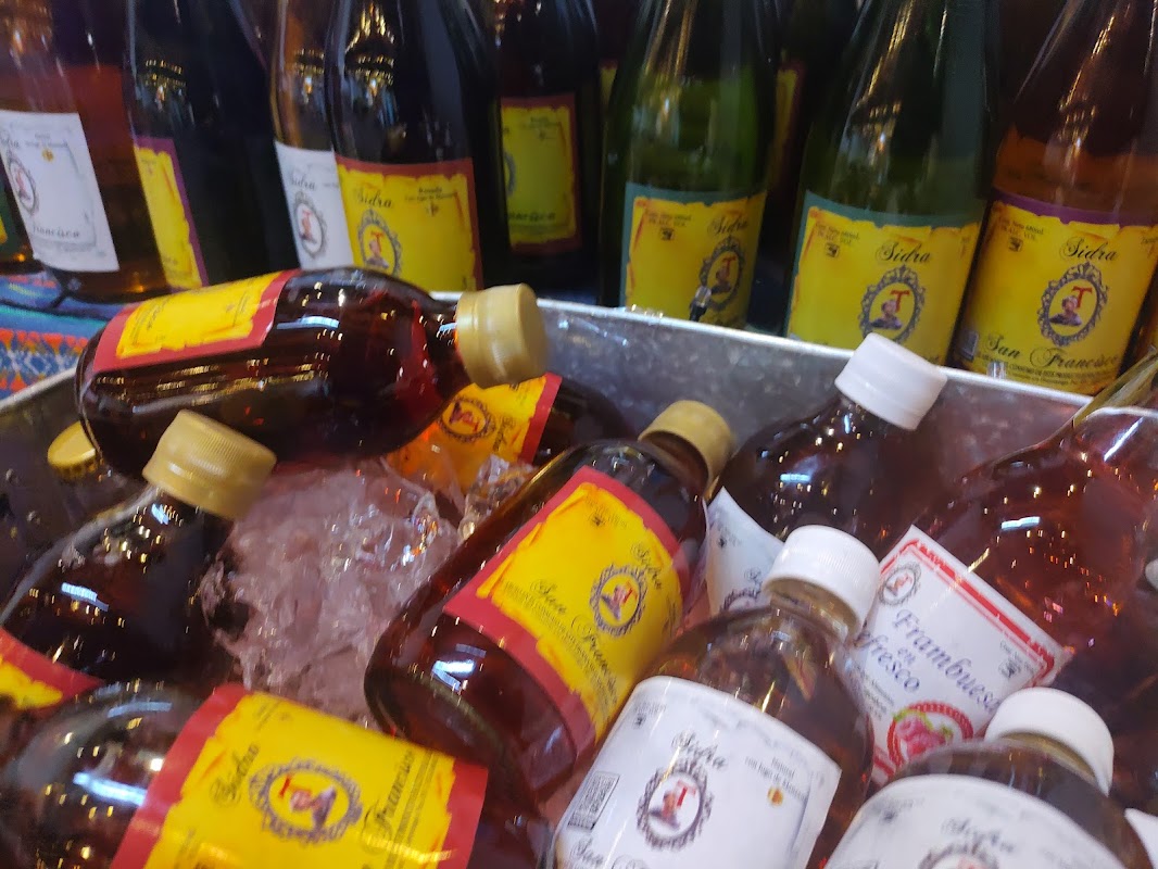 Mostrador de Sidra San Francisco con botellas de sidra alineadas y una copa de sidra de guayaba en primer plano