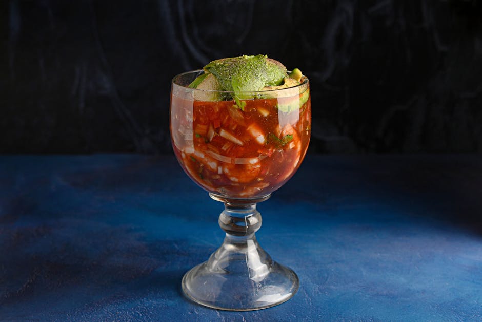 A refreshing glass of Mexican ceviche with avocado garnish on a dark background.