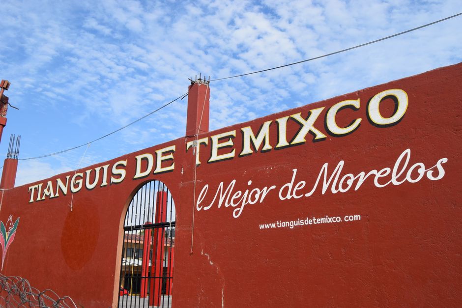 Red wall with Tianguis de Temixco signage against a bright blue sky, entrance visible.