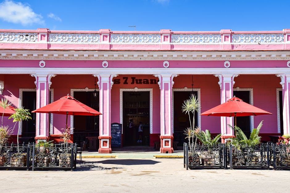 Sunlit pink café with red umbrellas in Remedios, Cuba, showcasing colorful colonial architecture.