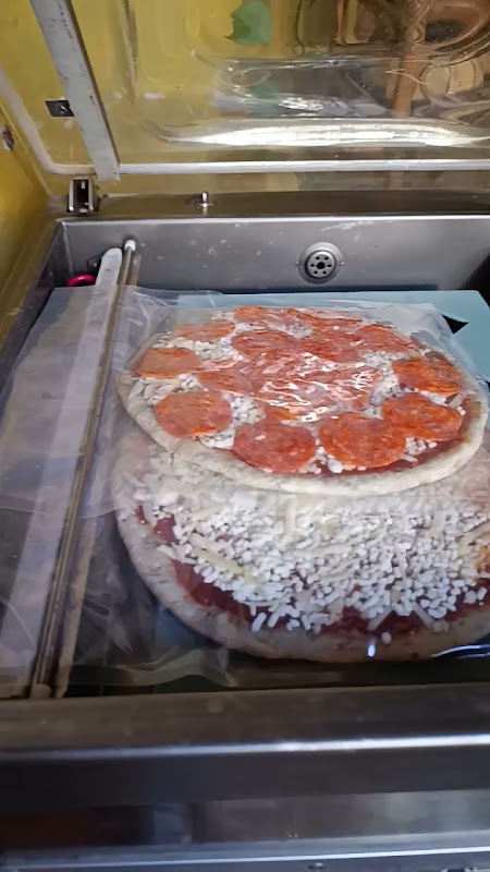 Exterior de Dinonni Pizza Mesón italiano con letrero rojo y una mesa al aire libre, mostrando una pizza recién salida del horno
