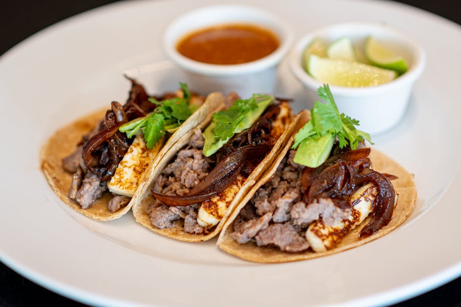 Delicious tacos filled with meat, cheese, onions, and cilantro, served with lime and sauce.