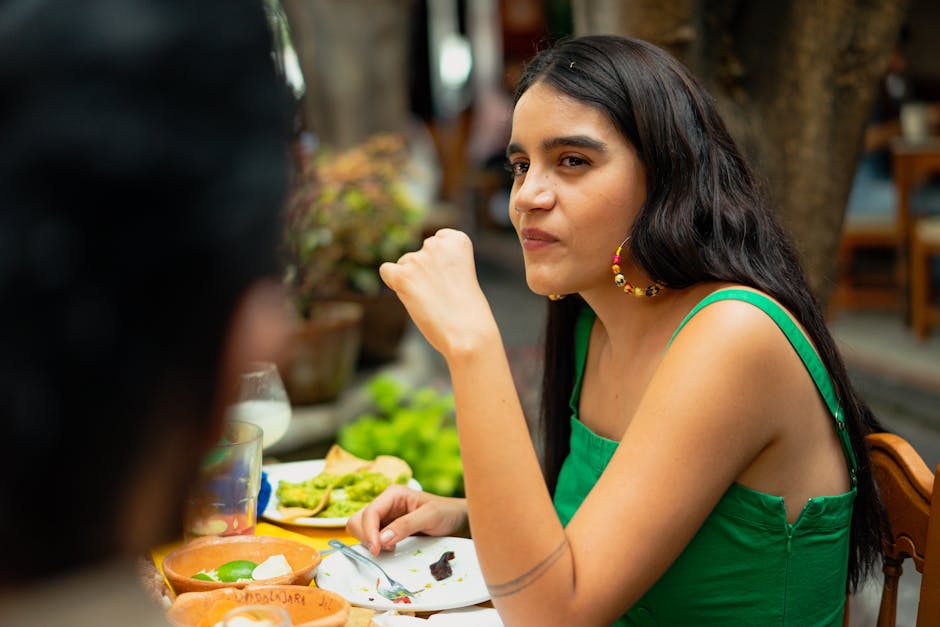 Young woman in green top dining outdoors, enjoying delicious Mexican food on a sunny day.