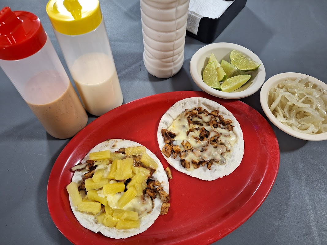 Fachada de Tacos Árabes Harbanos en Calle 13, con luces nocturnas y clientes en la acera