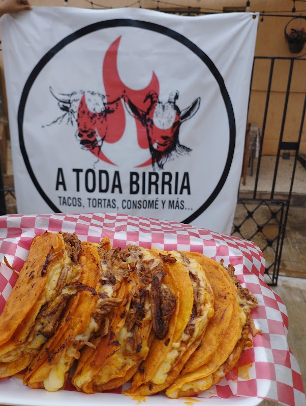 Tacos de birria con consomé humeante en A Toda Birria, mostrados en un plato de cerámica