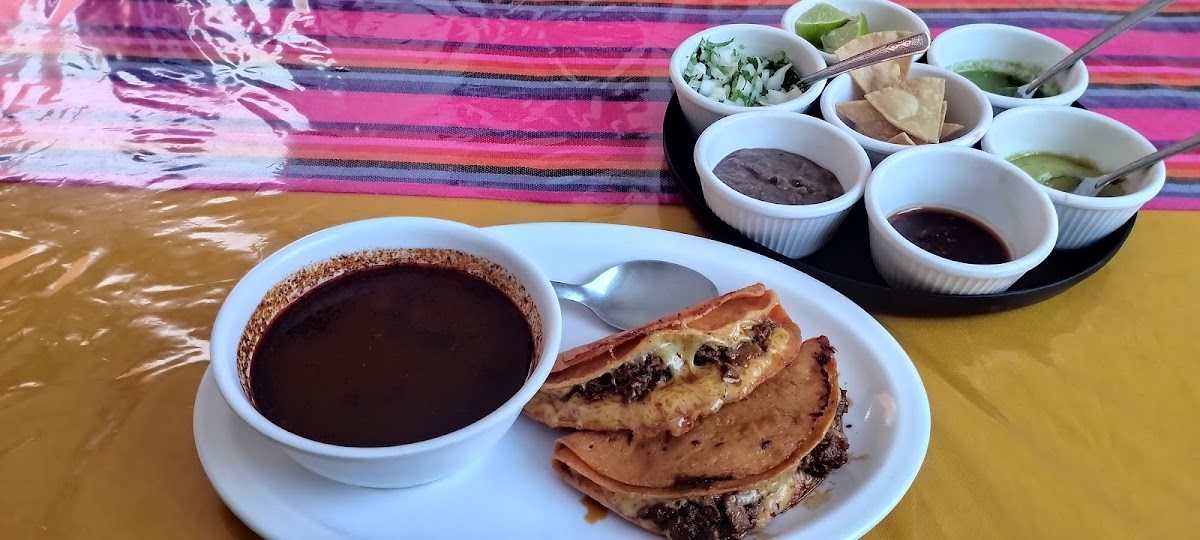 Interior con mesas de madera y aire acondicionado en A Toda Birria, gente disfrutando su comida