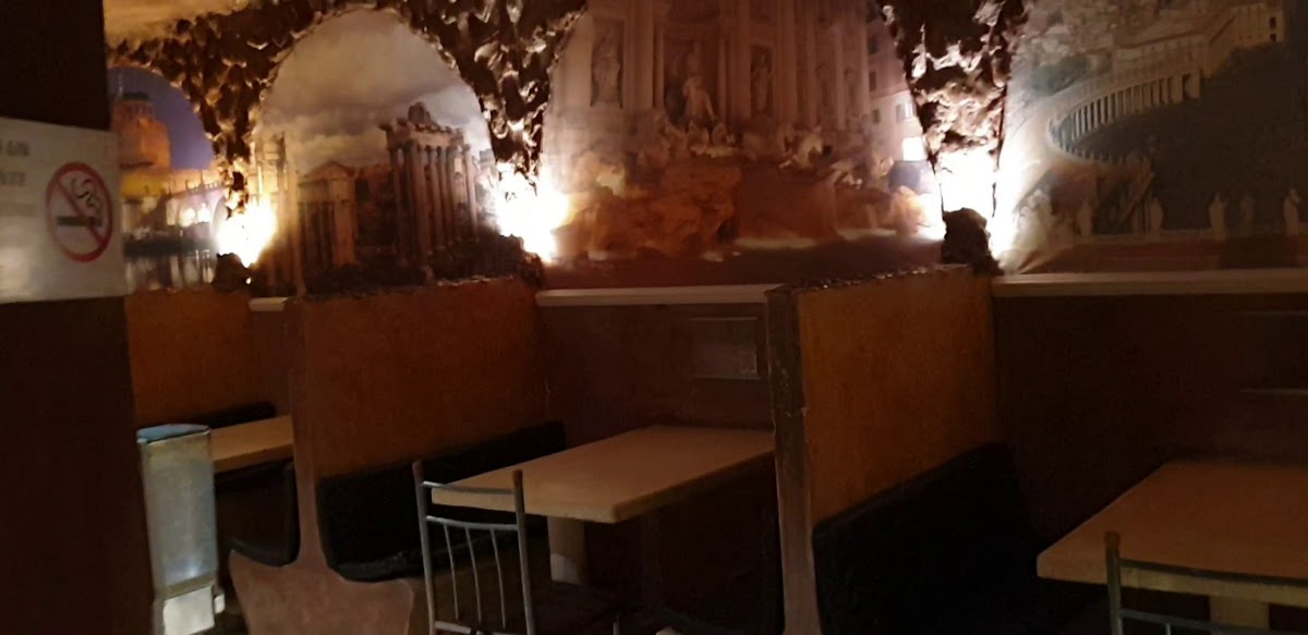 Exterior de Antica Roma con su fachada iluminada y mesas al aire libre, mostrando una botella de vino y platos de pasta en primer plano