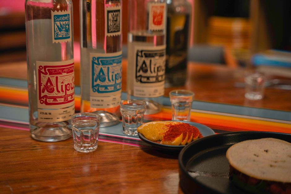 Colorful close-up of mezcal bottles with orange slices and shot glasses, perfect for bar scenes.