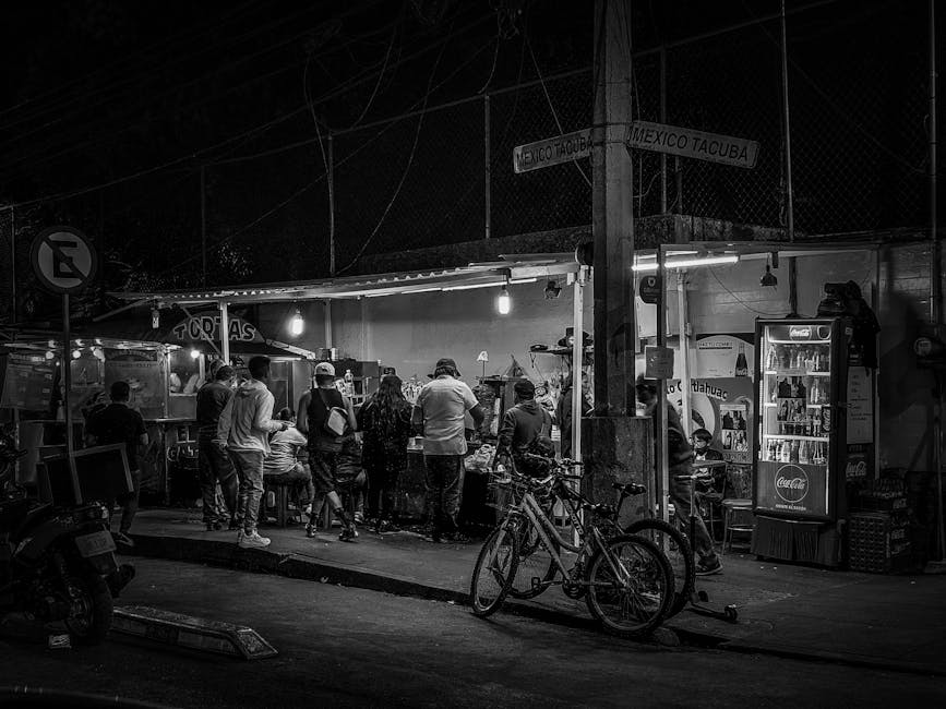 Black and white photo capturing people gathered at a bustling street food stall at night.