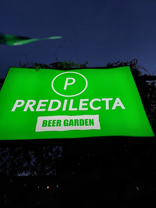 Jardín al atardecer con mesas al aire libre y cervezas artesanales en Predilecta Beer Garden