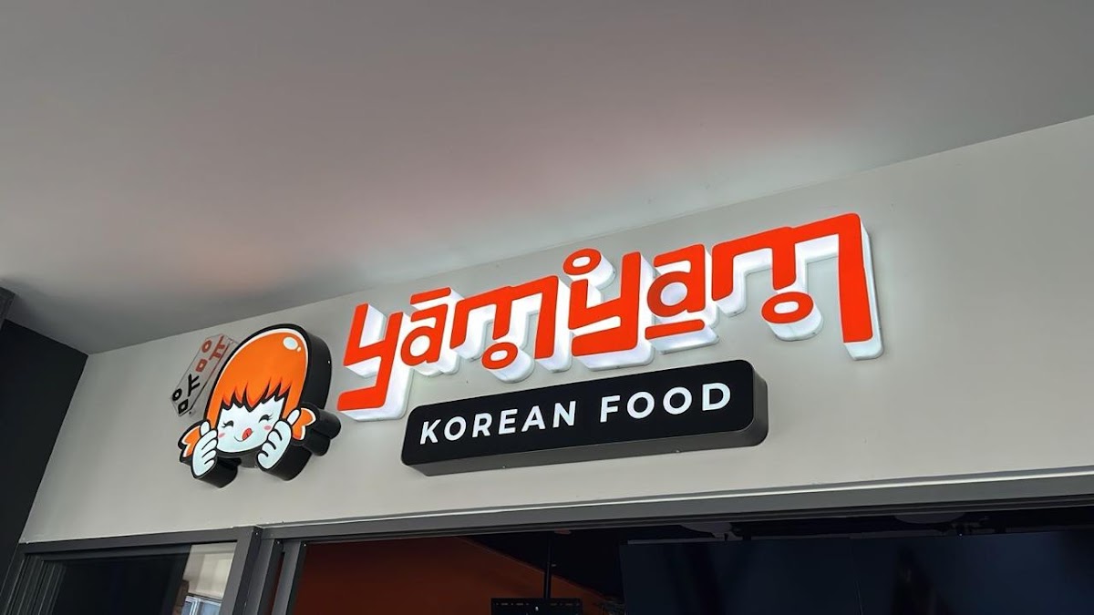 Interior de YamYam con mesas de madera, luces colgantes y una pared decorada con dibujos de hanboks