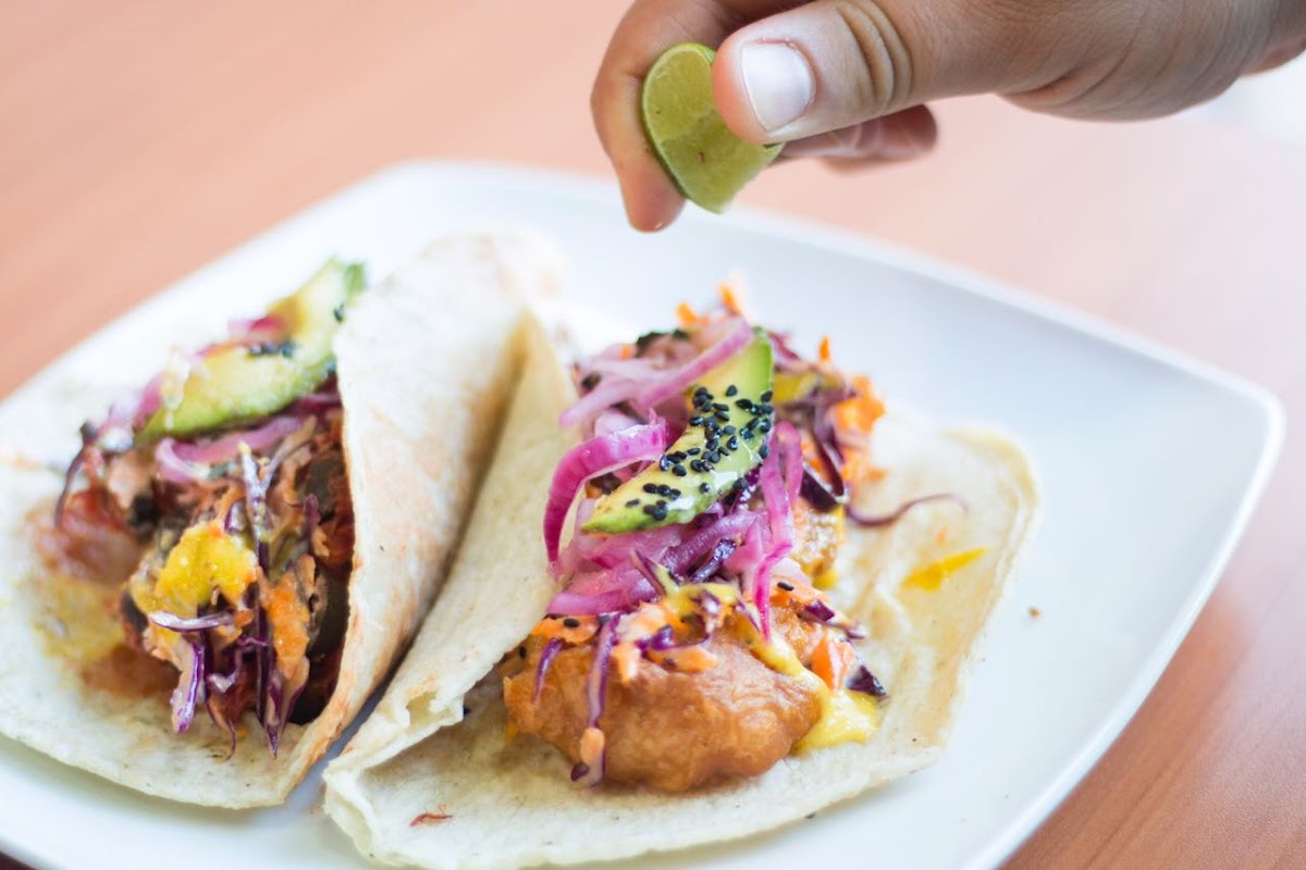 Primer plano de tacos de pescado crujientes con salsa de chipotle en una tabla de madera, en Patmos Cocina de Mar