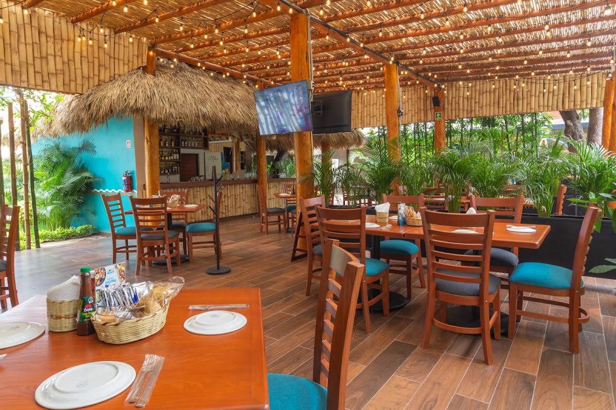 Vista frontal de Coco Beach Reforma con su letrero azul, mesas al aire libre y camarones a la parrilla en primer plano