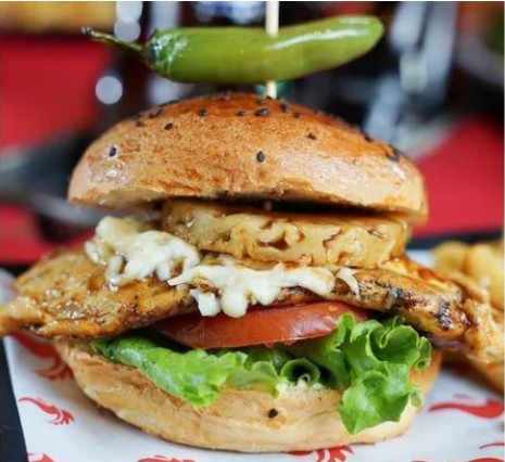 Gallo Cervecero SportsBar – burger jugoso y michelada en la mesa, interior con pantallas y fútbol