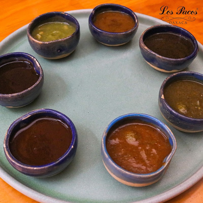 Tlayuda de mole negro con queso Oaxaca y chapulines en una tabla de madera, enfoque cercano del plato en Los Pacos
