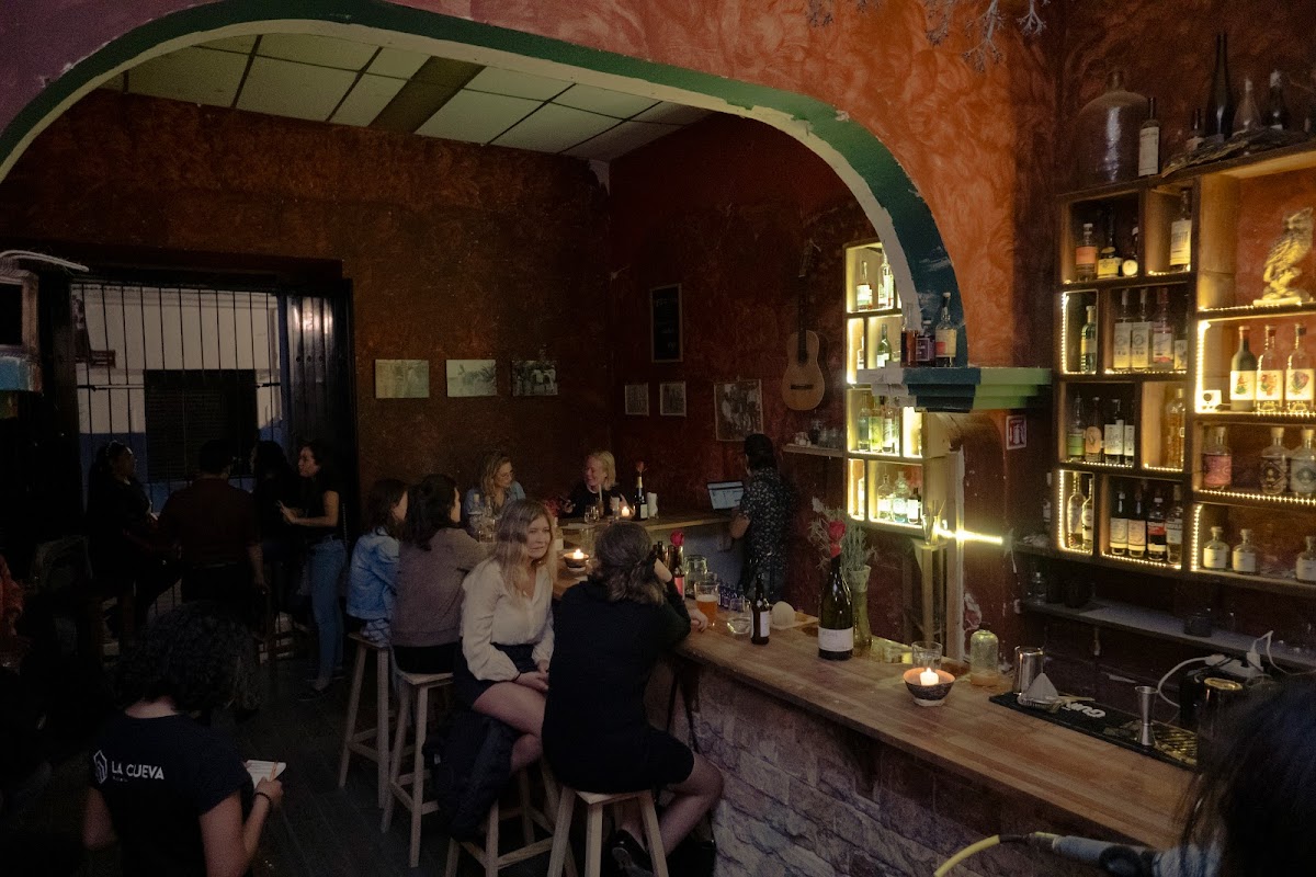Interior de La Cueva Oaxaca con barra de madera, botellas de mezcal alineadas y clientes conversando