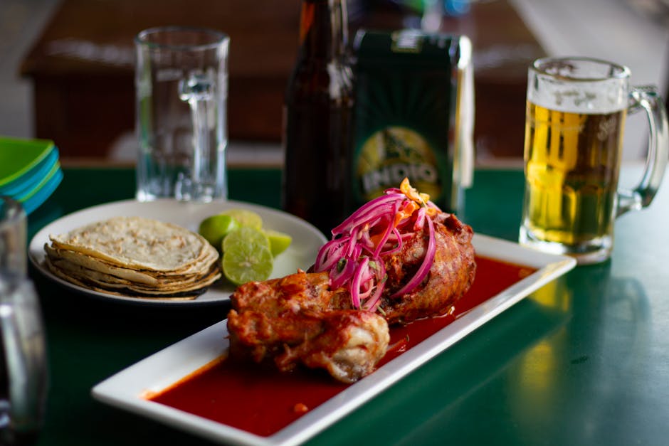 Close-up of a traditional Mexican meal with beer, featuring meat, sauce, and tortillas.