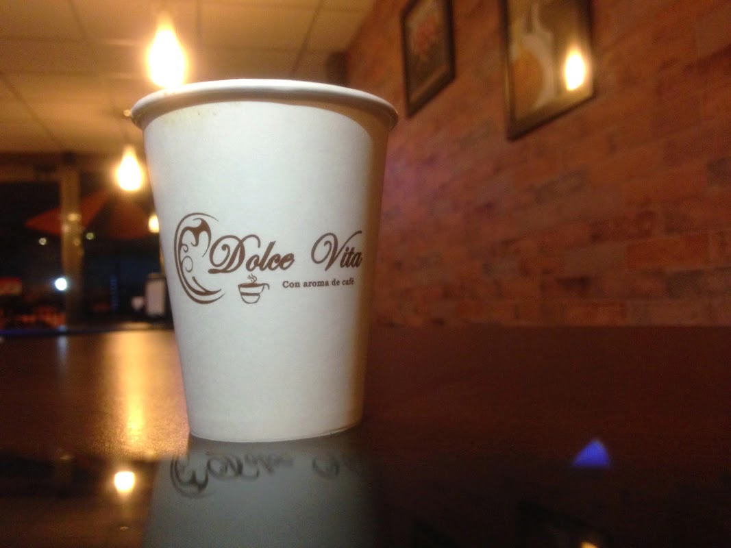Interior de Dolce Vita Coffee, mesas de madera y barra con taza de cappuccino humeante