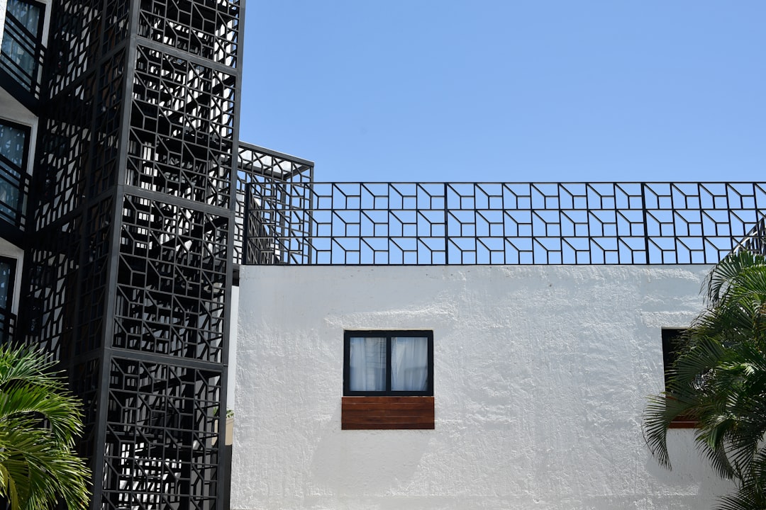 Modern white building with black geometric railing against blue sky.