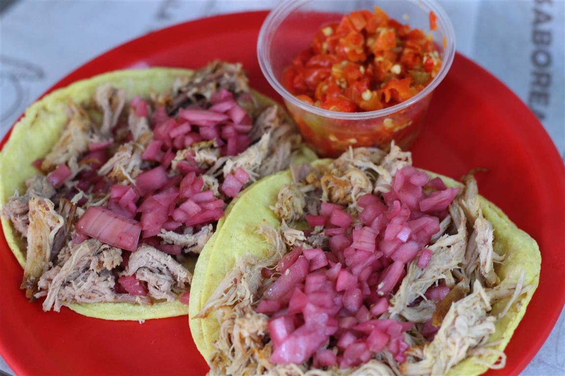Taquería El Naranjo (Suc Mercado) — puesto de tacos en la calle 27, tacos de cochinita pibil en plato de papel, señal del mercado