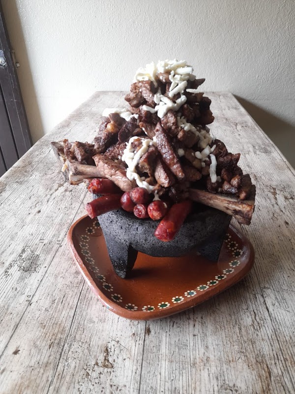 Los Molcajetes con su molcajete de piedra sirviendo un guiso de carne, interior rústico y mesas de madera