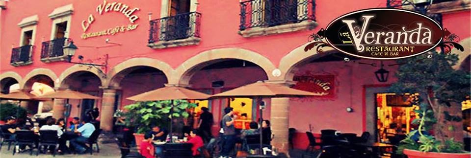 Fachada colonial de La Veranda con mesas al aire libre y una botella de mezcal sobre la mesa