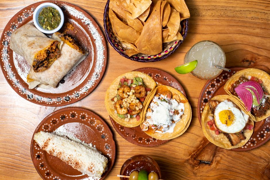 Savor a delicious spread of authentic Mexican tacos, burrito, and refreshing drink on rustic wood table.