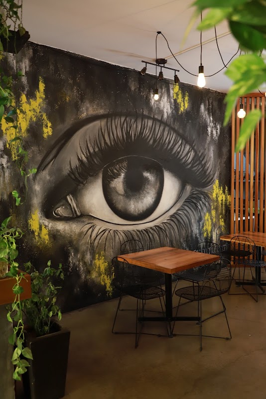Interior de Café Sideral: barra de madera, luces colgantes y plantas verdes, con barista preparando un café