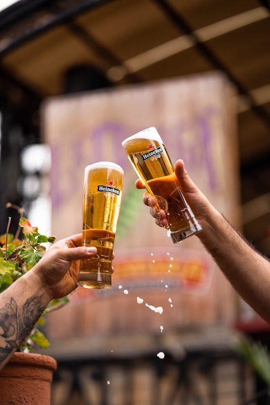 La Oruga y La Cebada — terraza con barriles de cerveza artesanal, clientes disfrutando de una michelada y vista del menú en una pizarra