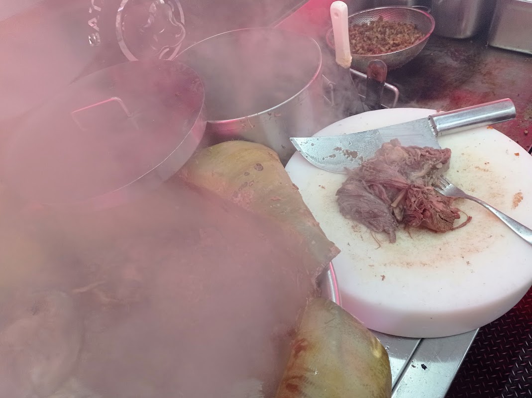 Interior del local mostrando el mostrador, el taquero en acción y la fila de clientes en Tacos El Torito