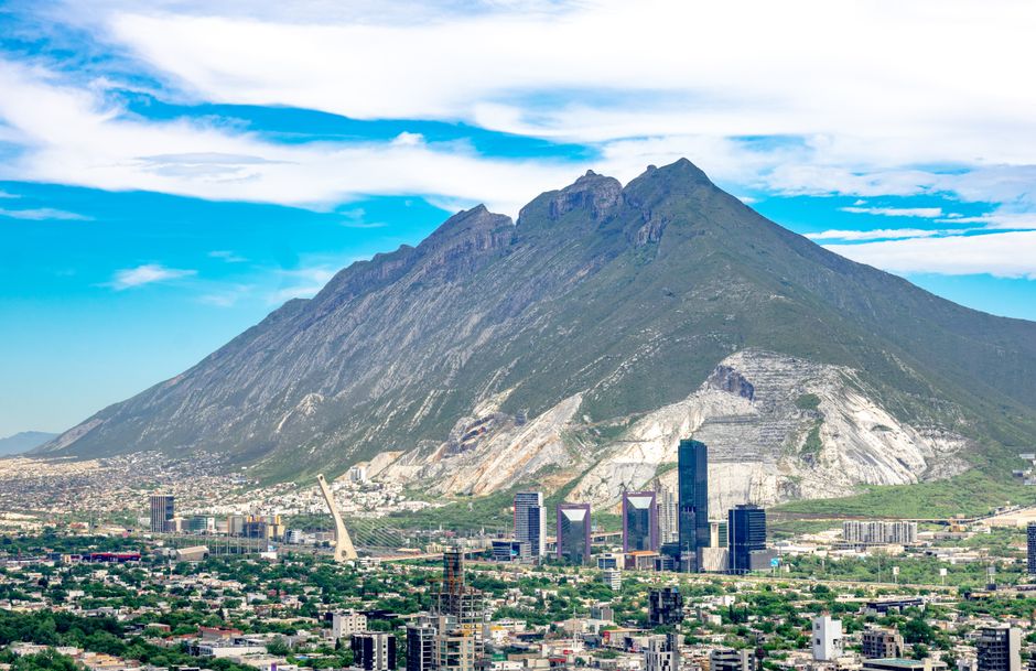 Panoramic aerial view of Monterrey cityscape with the iconic Cerro de la Silla mountain in the background.