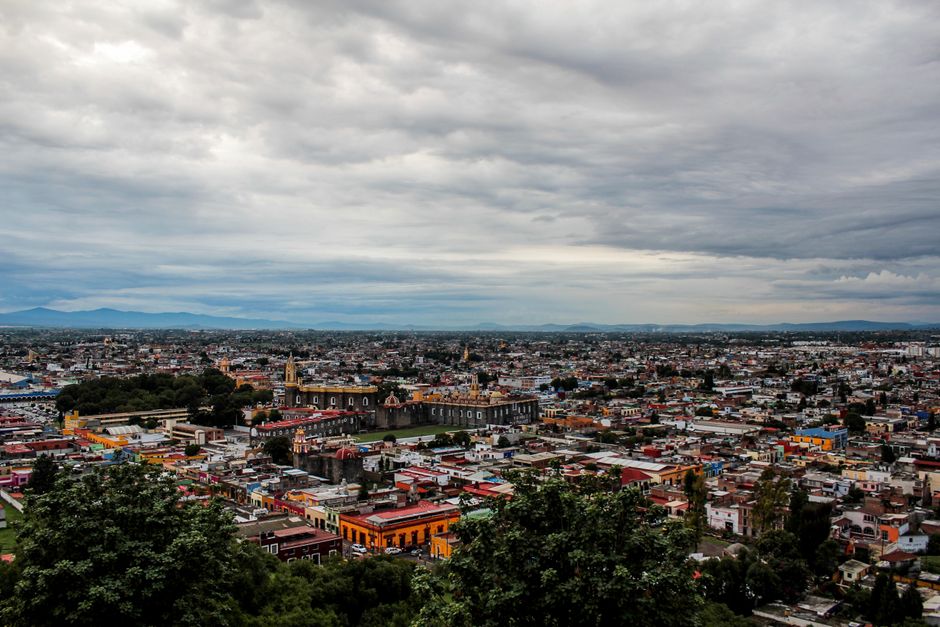 Aerial view of vibrant Cholula cityscape showcasing colorful buildings under a cloudy sky.