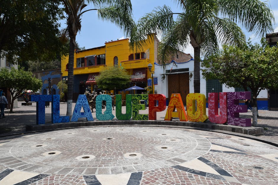 Vibrant Tlaquepaque sign in a lively Mexican plaza with palm trees and buildings.