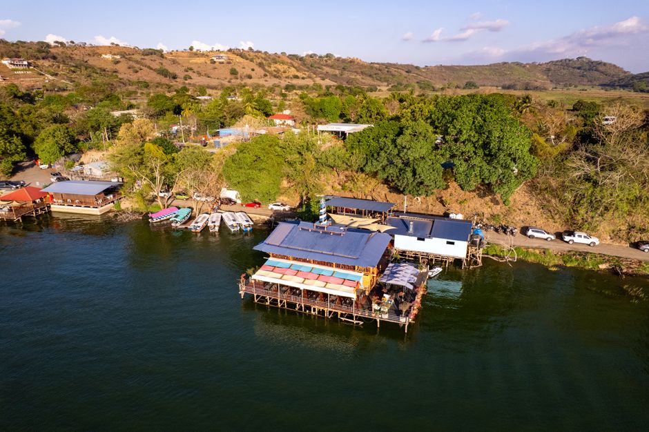 Aerial photograph of a lakeside restaurant in Apastepeque, El Salvador, with lush surroundings.