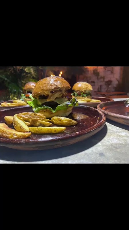 Primer plano de una hamburguesa jugosa de T‑O‑X Central de hamburguesas, con queso fundido y papas fritas al lado.