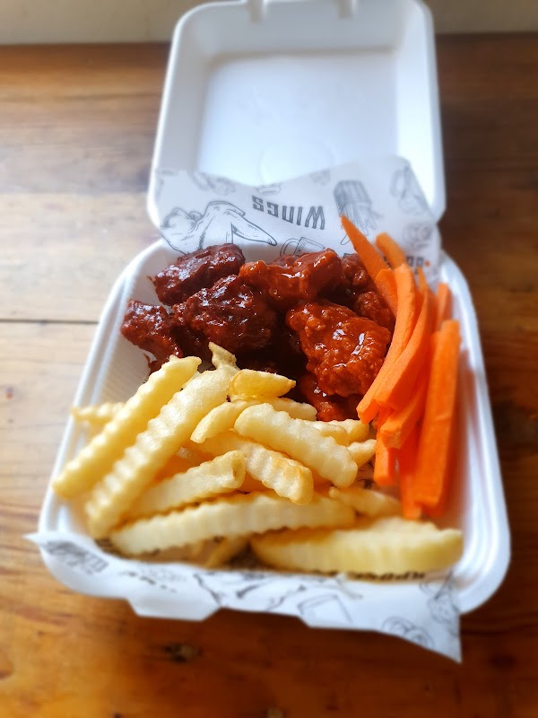 Chutis wings — alitas cubiertas de salsa picante, servidas en una bandeja con papas fritas, ambiente de barra