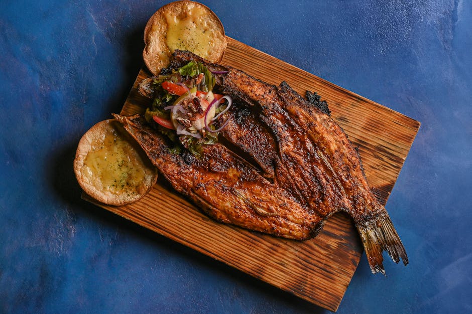 Delicious grilled fish served on a wooden platter with fresh vegetable toppings and bread side.