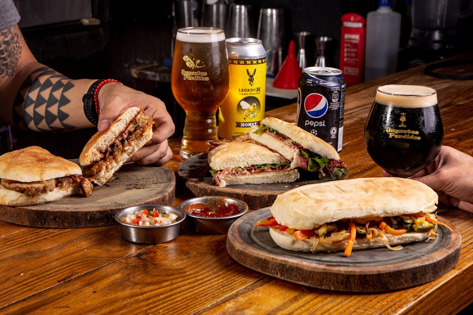 Close-up of gourmet sandwiches paired with craft beers on a rustic wooden table.