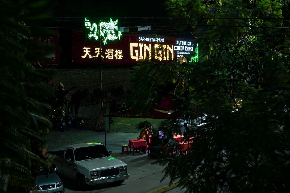 Vibrant nightlife scene in Mérida, showcasing a neon-lit street with parked cars and people enjoying dinner.