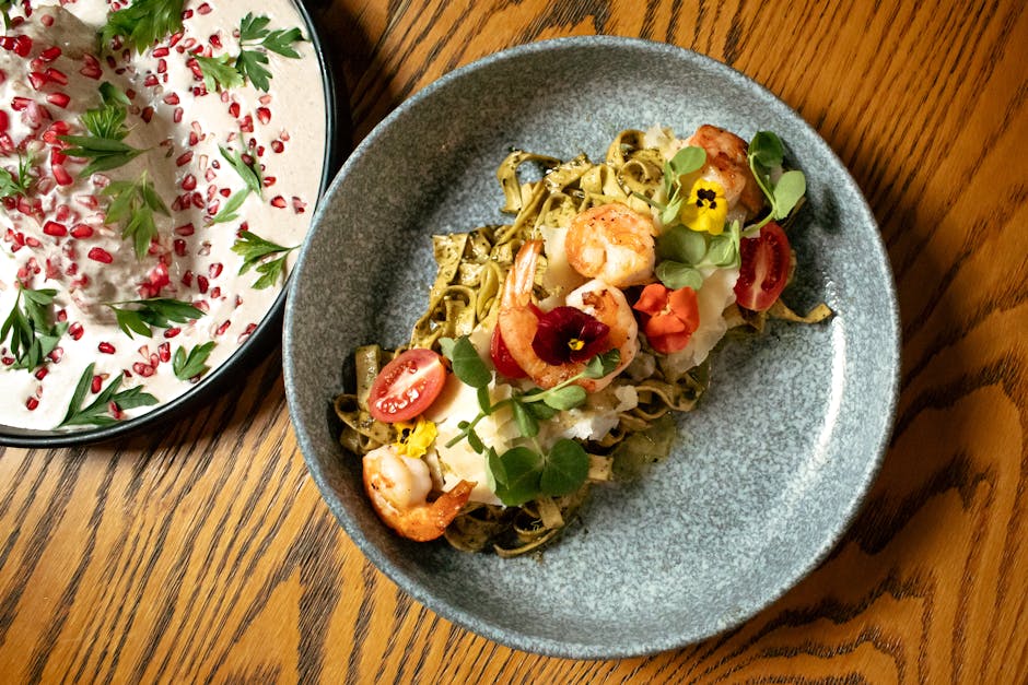Elegant pasta topped with shrimp, edible flowers, and greens on a wooden table.