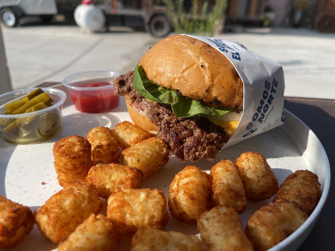 Hamburguesa North Burger con queso fundido, cebolla caramelizada y salsa de adobo en plato de madera, primer plano