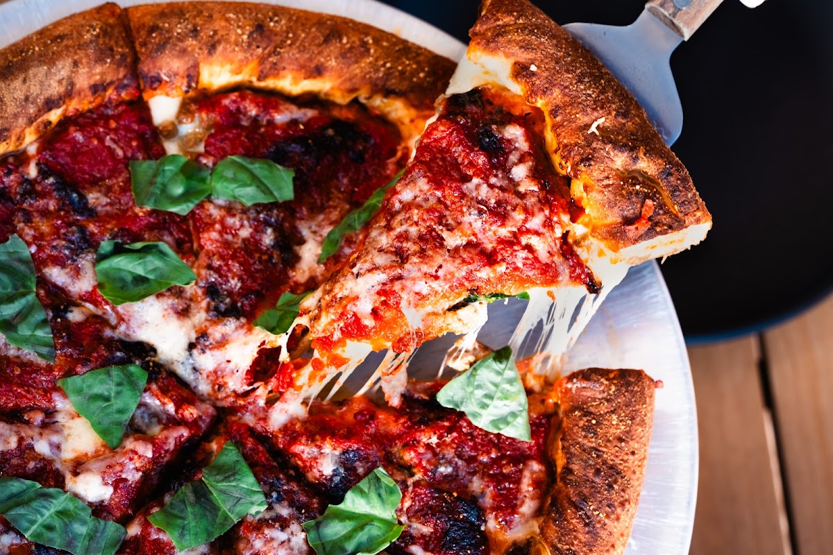 Deep‑dish pizza de Ruta Uno, masa crujiente, salsa roja, pepperoni y queso fundido, servida en tabla de madera — primer plano