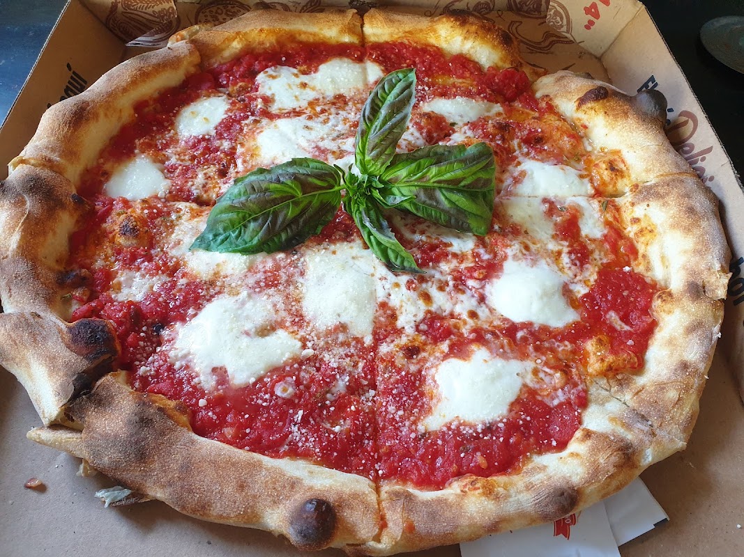 Interior industrial de Al Forno con pizza estilo Detroit en primer plano y cócteles en la barra
