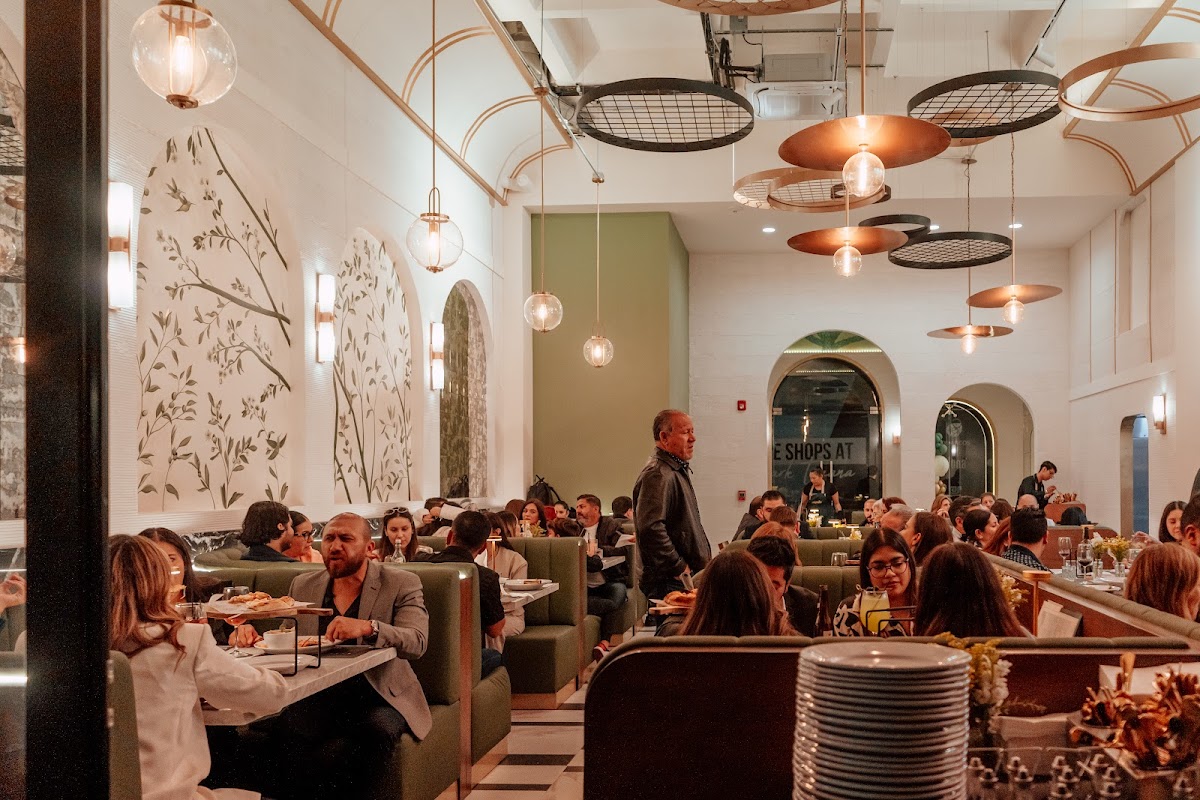 Interior del restaurante con mesas de madera, luces cálidas y clientes disfrutando de platos de pasta