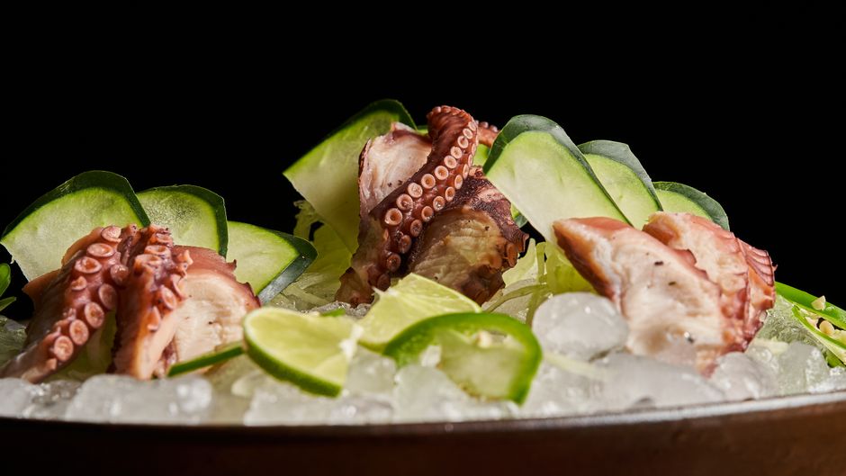 Sliced octopus tentacles garnished with lime and cucumber on ice, perfect for a seafood dish.
