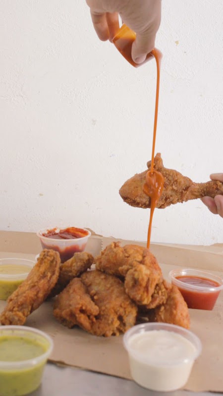 Primer plano de las alitas crujientes de Croonchy en un plato de cerámica, con salsa brillante y guarnición de limón