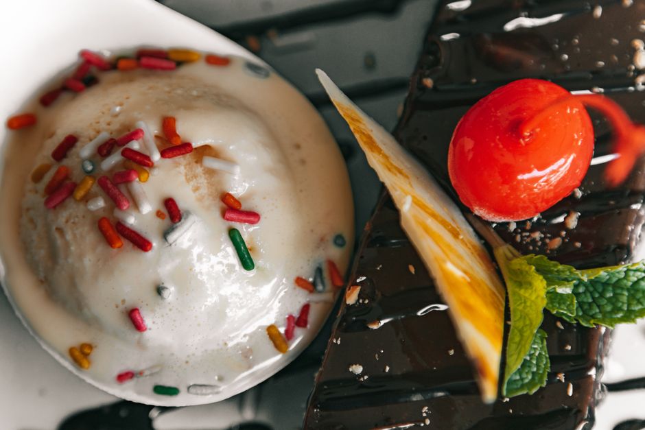 Delicious ice cream with sprinkles and chocolate dessert garnished with cherry and mint.
