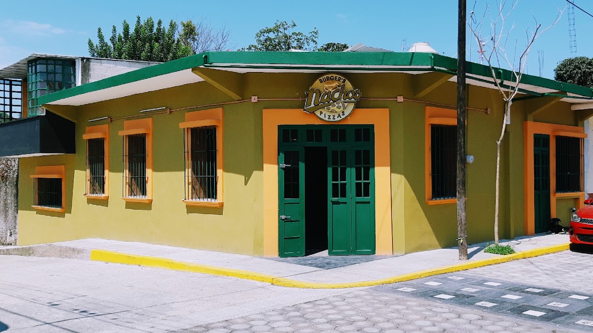 Nacho's Burgers & Pizzas — exterior con letrero colorido y una mesa con hamburguesas y porciones de pizza bajo luz natural
